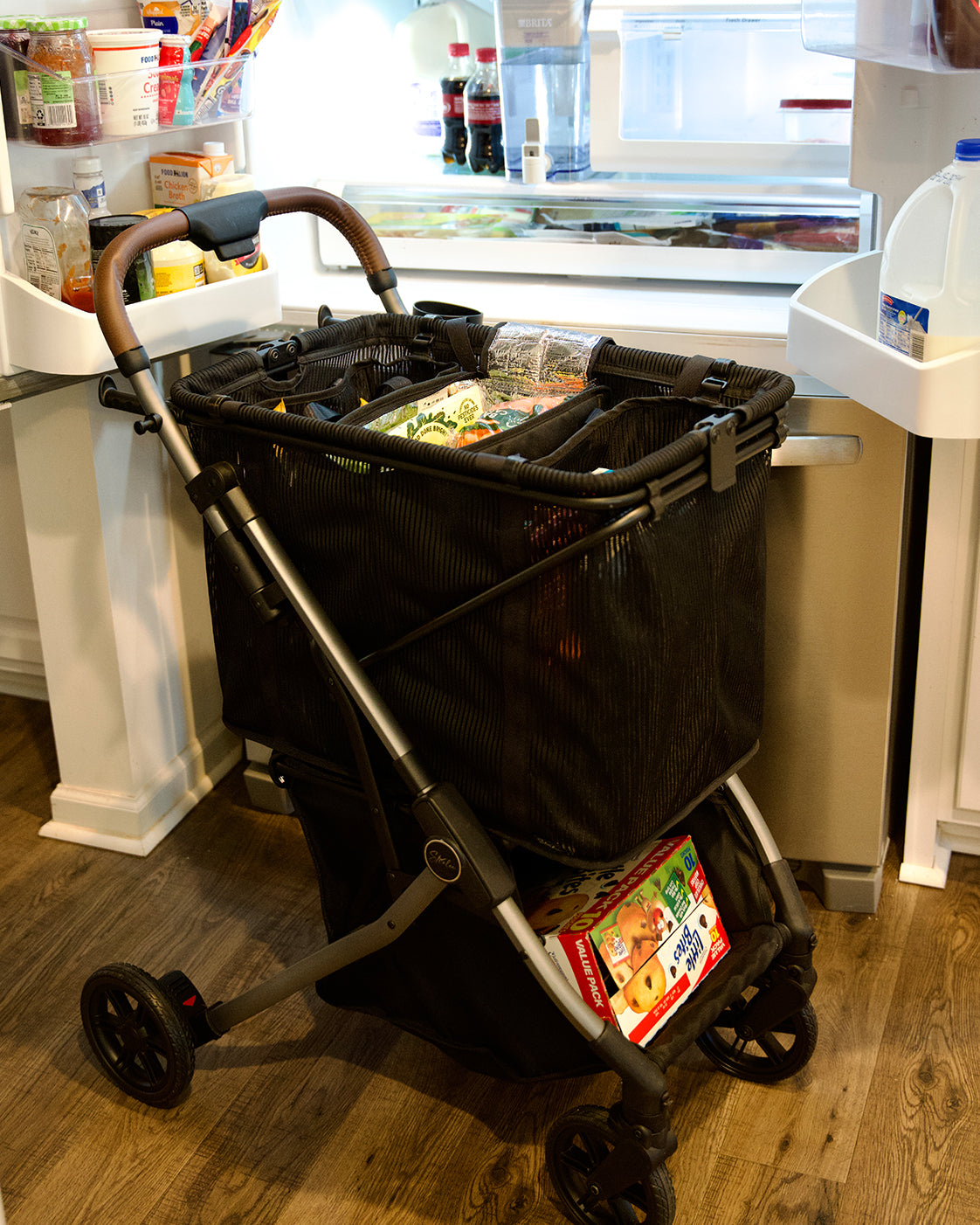 Strolee cart filled with groceries beside an open fridge.