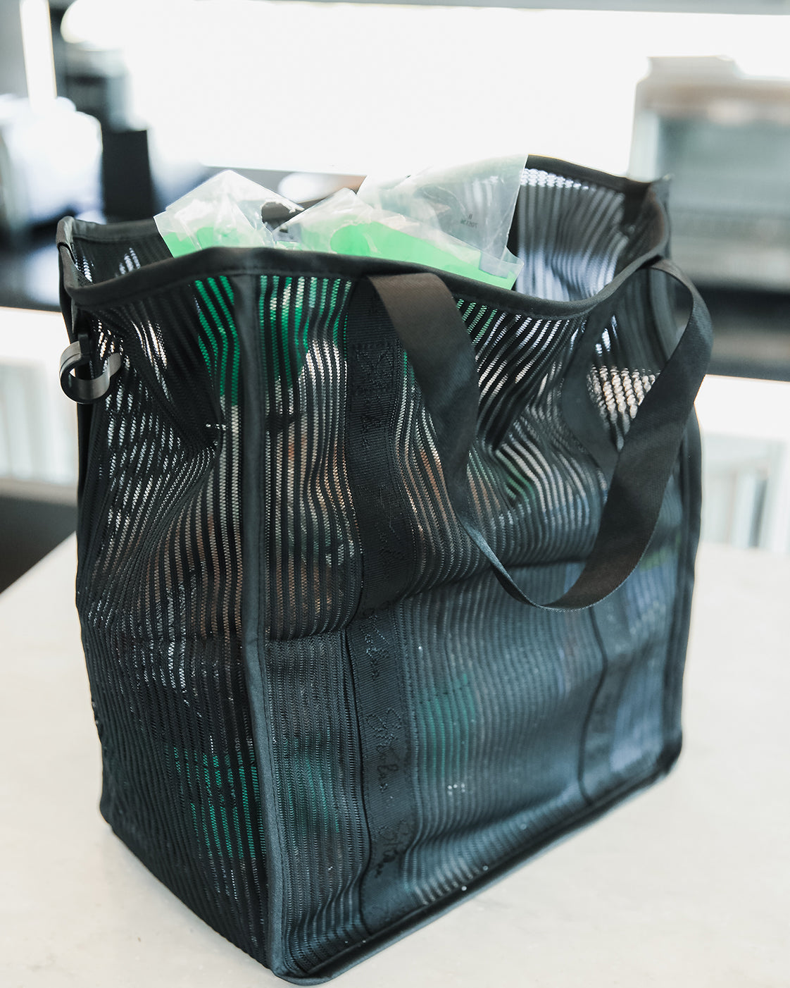 Vue de côté d’un sac de rangement en maille rempli et de ses poignées de transport sur un plan de travail.