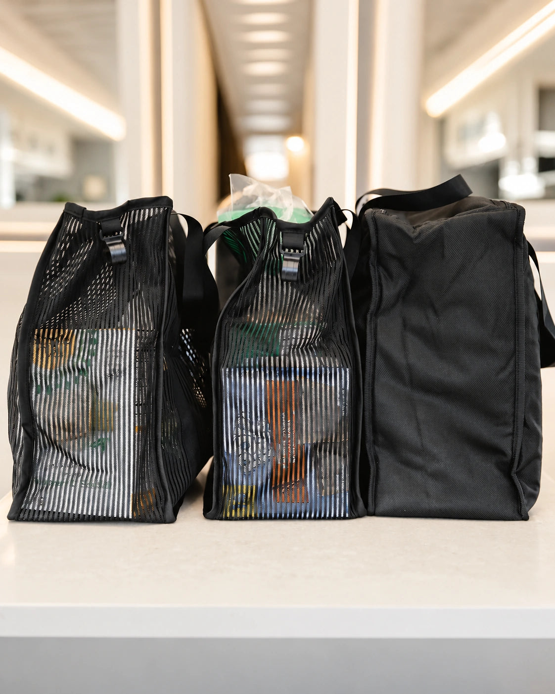 Deux sacs de rangement en maille remplis et un Insulated Freezer Bag, coloris Black, posés sur un plan de travail de cuisine.