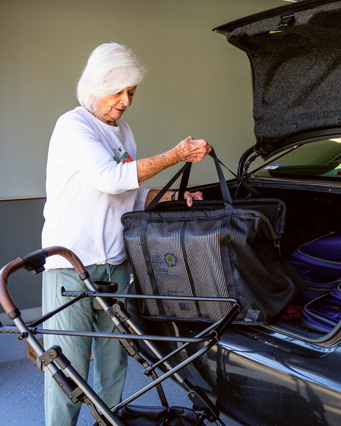 Frau hebt neben einem Stability Shopper eine Einkaufstasche zum offenen Kofferraum eines Autos.